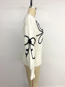 Détail d'un pull en maille blanc avec broderie 3D noire et finitions côtelées