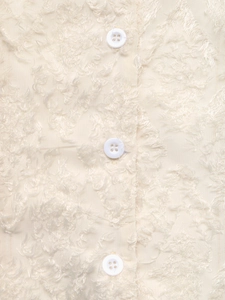 Detailed view of white shirt fabric with textured eyelash fringe and round resin buttons