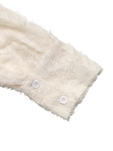 Detailed close-up of cream shirt cuff with unique textured fringe fabric and buttons