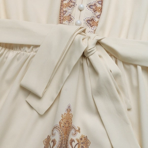 Gros plan sur la broderie ethnique et la taille ceinturée d'une robe longue beige