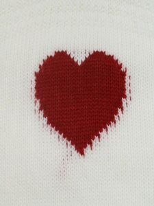 Detailed close-up of knitted fabric texture with red heart jacquard pattern on white sweater