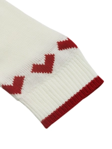 Detailed macro view of the cream knit sweater cuff featuring a red woven heart pattern