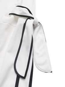 Close-up of a white bow tie with black contrast piping detail on a women's striped sweatshirt