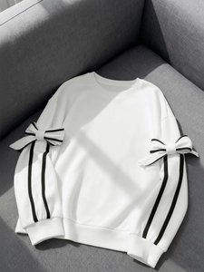 Close-up of white sweatshirt with black side stripes and 3D bow detail on sleeves