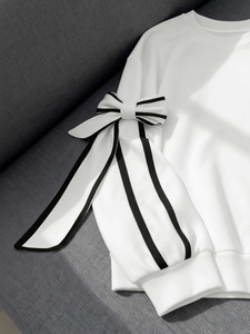 Detailed view of white sweatshirt featuring large striped bow and ribbon on sleeve