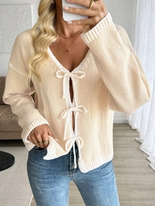 Détail d'un cardigan beige en maille avec des nœuds blancs et des bordures contrastées