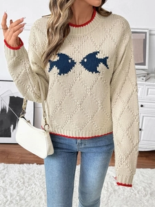 Détail de la texture tricotée et du motif de poisson bleu sur le pull crème