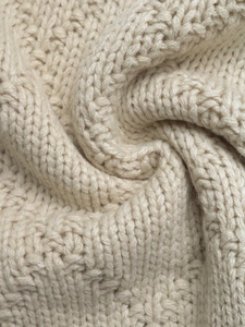 Vue macro de la texture du pull en maille épaisse crème montrant les fils tressés