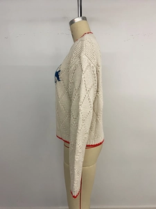 Détail des bordures contrastées et du tricot à losanges sur le pull crème à manches longues