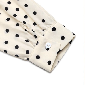 Détail de la manche d'une robe à pois blancs avec bouton et plis délicats au poignet