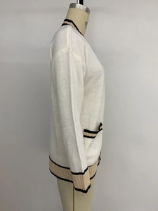 Detail of white knit cardigan showing contrast striped trim on the pocket and sleeve cuff