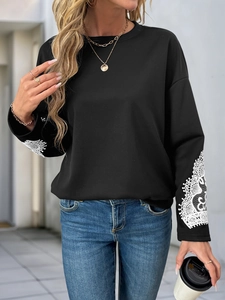 Detailed close-up of white lace hollow embroidery on the cuffs of a black crewneck sweatshirt