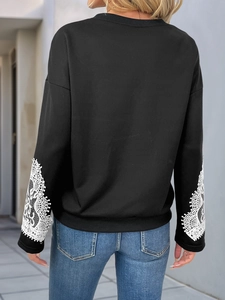 Detail of white lace embroidery on sleeves of a black crewneck sweatshirt for women