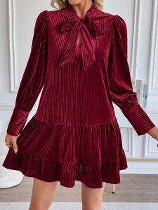 Détails d'une robe en velours plissé bordeaux avec col à nœud et ourlet à volants