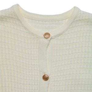Close-up of cream knit cardigan featuring waffle texture and vintage gold crest buttons