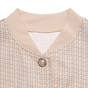Gros plan sur la veste en tweed beige montrant le tissage texturé et le bouton doré