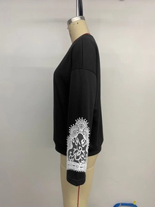 Detail showing the white lace embroidery pattern on the sleeve of a black crewneck sweatshirt