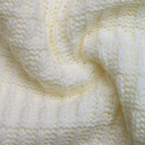 Close-up detail of cream white cable knit fabric with thick wool texture and soft folds