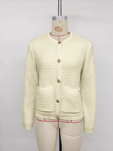 Detail of cream knit cardigan with golden buttons and vertical ribbed texture