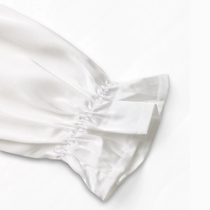 Detail of white satin long sleeves featuring elastic ruffled cuffs and smooth fabric texture