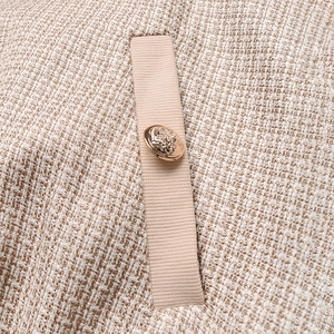 Détail du tissu en tweed de la veste avec bord-côte et bouton doré à relief de type Méduse