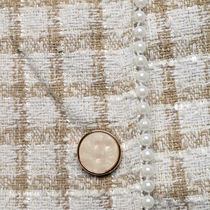 Detail of tweed fabric texture with pearl bead trim and a gold-rimmed button on cardigan