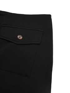 Detail of black straight skirt showing flap pocket with textured brown button and fine stitching