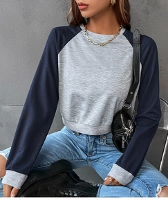 Detail eines grauen bauchfreien Sweatshirts mit dunkelblauen Raglanärmeln und Bündchen