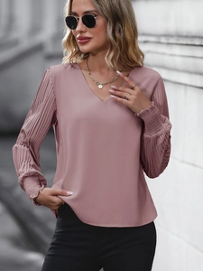 Détail des manches plissées et du col en V sur un chemisier élégant rose poudré