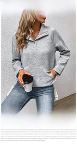 Detail eines grauen Sweatshirts mit geprägter Textur und Stehkragen mit Druckknöpfen