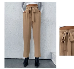 Detail of khaki high waist trousers showing the adjustable belted waist and pleated fabric