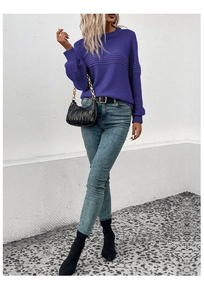 Outdoor shot of a woman in a dark purple knit sweater with textured stripes and blue jeans