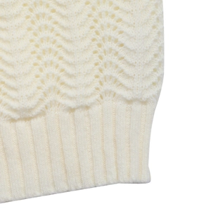 Detail of cream white knit sweater showing wavy hollow patterns and ribbed cuff texture