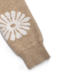 Detailed macro view of camel knit sweater sleeve with white daisy floral pattern and ribbed cuff