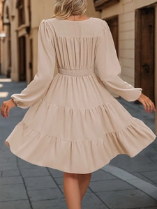 Detail of tiered skirt hem and elastic high waist on long sleeve beige dress