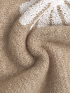 Detailed macro view of camel knit sweater with soft white floral patterns and rich textures