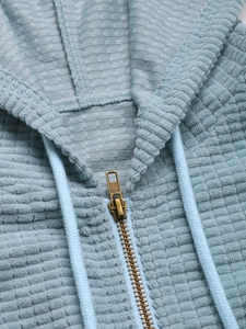 Detail von hellblauem Waffelstrick-Hoodie mit Vintage-Metallreißverschluss und Kordelzug