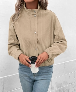Nahaufnahme der beigen Waffelstrickstruktur einer kurzen Cordjacke mit Stehkragen