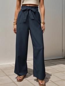 Close-up of navy paperbag waist pants with a self-tie bow and textured fabric details