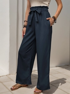 Detail of high-waist paperbag pants with elastic ruffled waist and matching tie belt