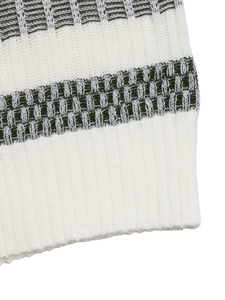 Detailed macro view of cream knit sweater with green geometric patterns and ribbed hem finish