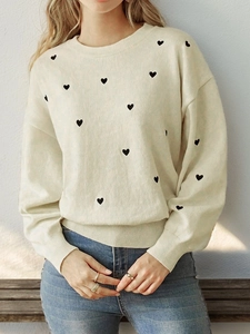 Detailed texture of ivory knit sweater with black heart patterns and ribbed cuff details