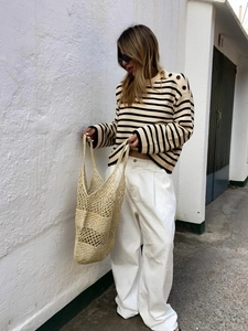 Detail of knit striped sweater featuring elegant shoulder buttons and woven handbag texture