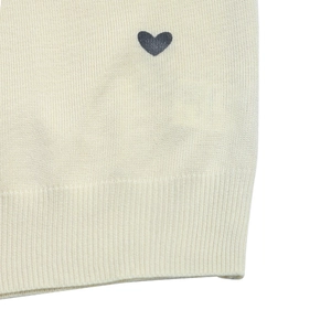 Detailed view of cream-colored knit sweater featuring dark grey heart motif and ribbed hemline