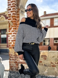 Schulterfreier Strickpullover mit Fischgrätenmuster und schwarze Kunstlederhose auf der Straße