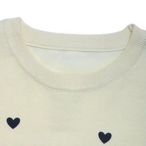 Detail of round neckline and black heart embroidery on cream knit sweater fabric