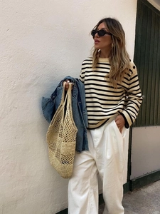 Close-up of a striped knit sweater paired with white wide-leg trousers and a straw tote bag