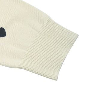 Detail of cream knit sweater cuff with ribbed texture and black heart embroidery