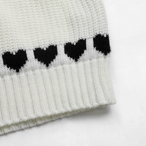 Macro shot of ribbed knit cuff with black heart jacquard pattern on white sweater