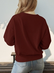 Close-up of the ribbed hem on a deep red knit sweater with blue washed denim jeans